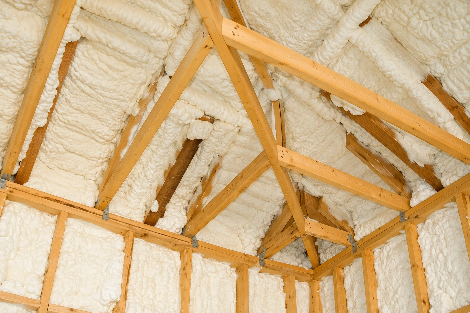 Cream-colored spray foam covers the roof and walls between exposed wooden framing.