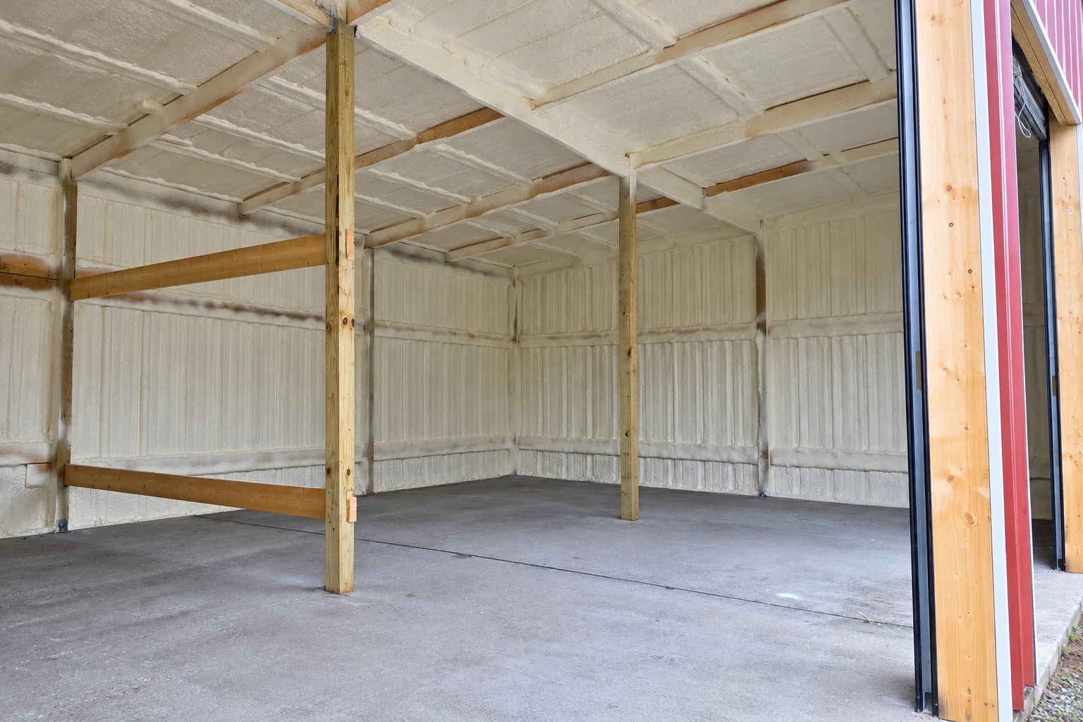 White spray foam insulation covers the walls and ceiling of a commercial space with exposed support posts and a concrete floor.