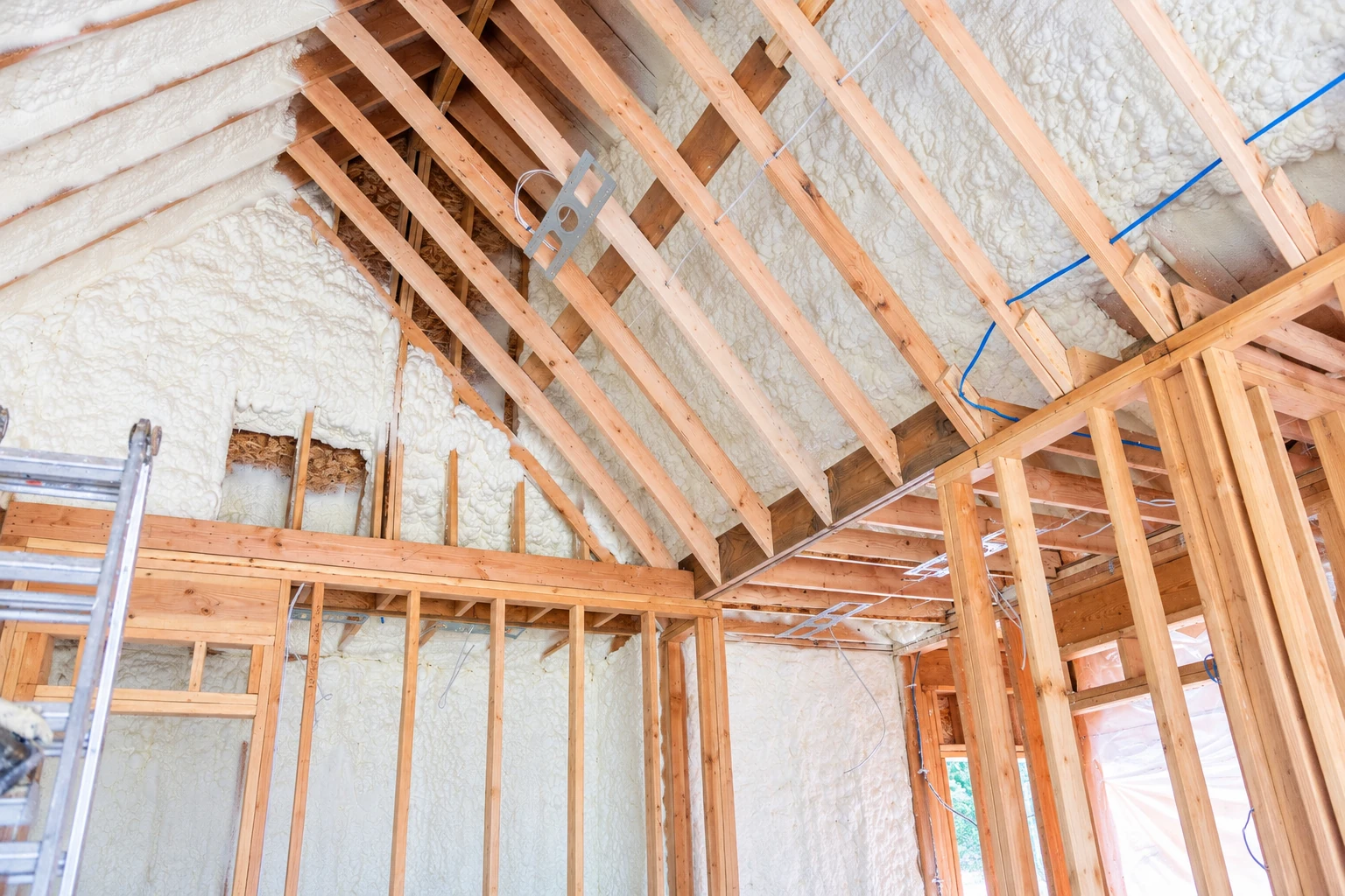 Open-cell foam insulation fills the roof and wall cavities of an unfinished home framed with exposed wooden rafters and studs.